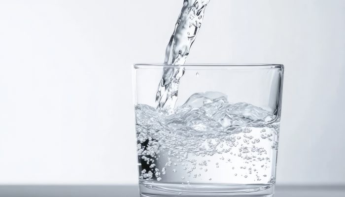 clear-water-being-poured-into-modern-designed-glass-against-solid-background